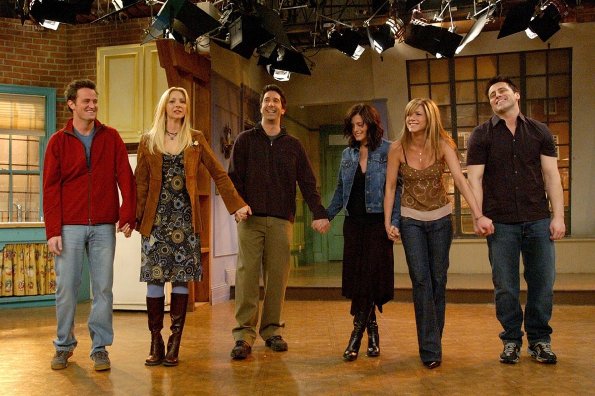 The cast members of friends standing in a cleared out set space holding hands, about to take a final bow.